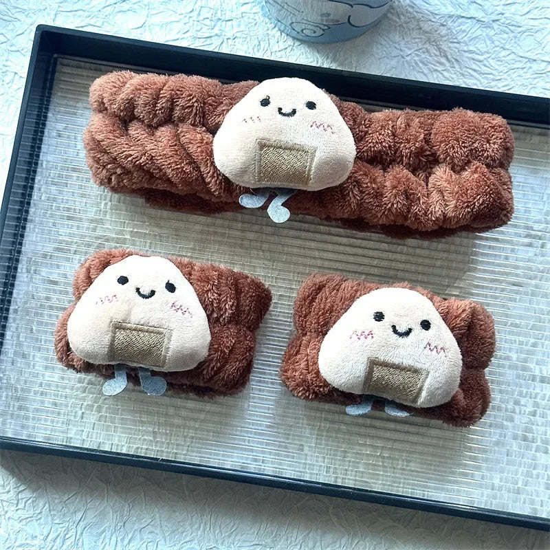 Três faixas de cabelo felpudas marrons com detalhes de oniguiri de pelúcia sorridente, sobre bandeja preta