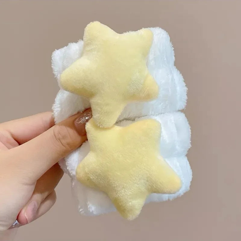 Mãos segurando elásticos de cabelo brancos com estrelas amarelas de pelúcia, fundo bege