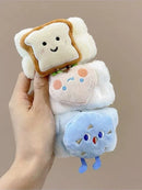 Mão segurando brinquedos de pelúcia fofos com rostos sorridentes: pão, morango e nuvem azul