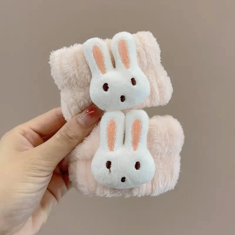 Mão segurando faixas de cabelo pelúcia rosa claro com rosto de coelho branco para cuidados faciais