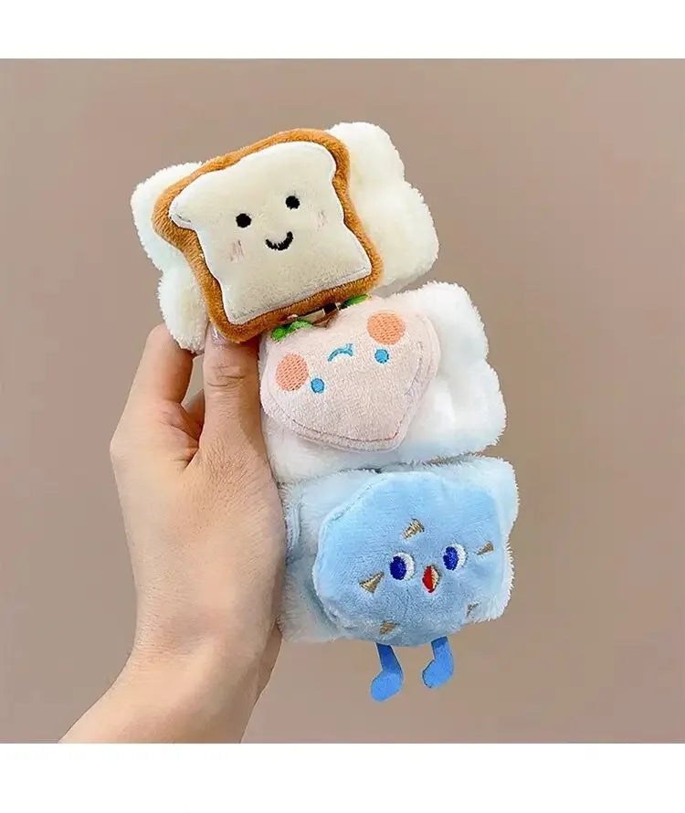 Mão segurando três pulseiras pelúcia branca com decoração de fatia de pão, morango e nuvem azul sorridentes