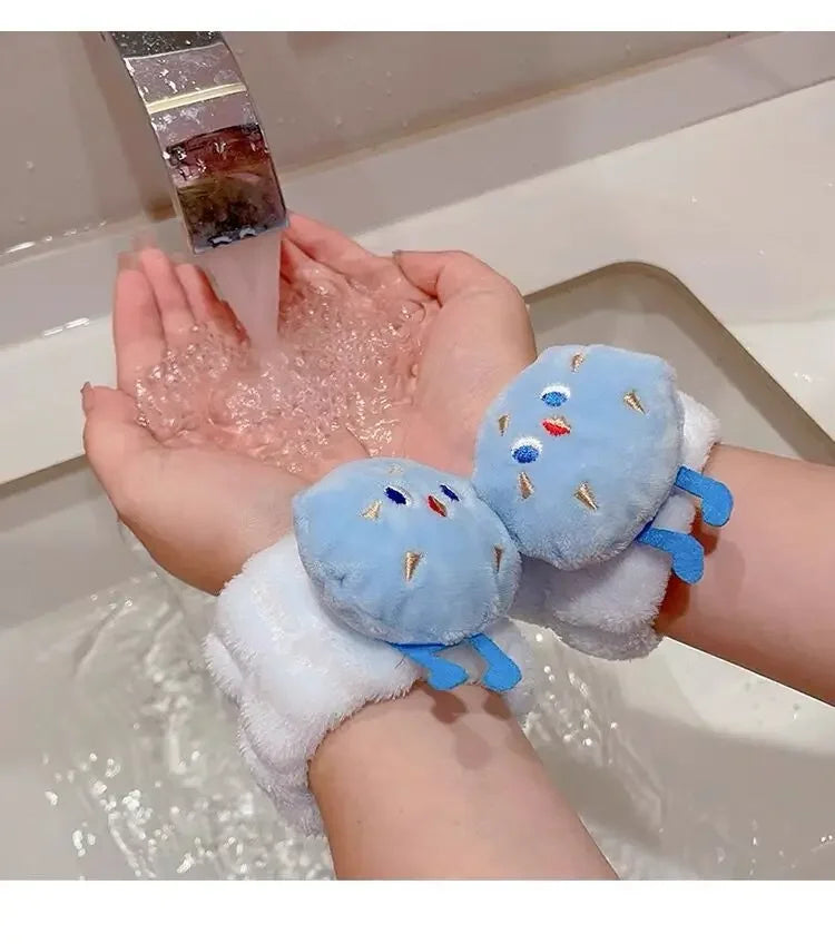 Mãos femininas sob torneira com água, usando acessórios de pelúcia azul em formato de personagem nos pulsos.