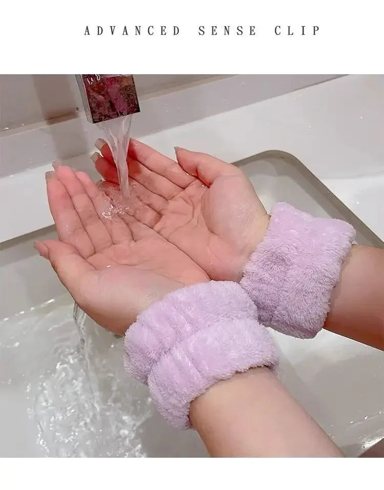 Mãos femininas sob torneira com água corrente, usando pulseiras felpudas lilás em pia branca.