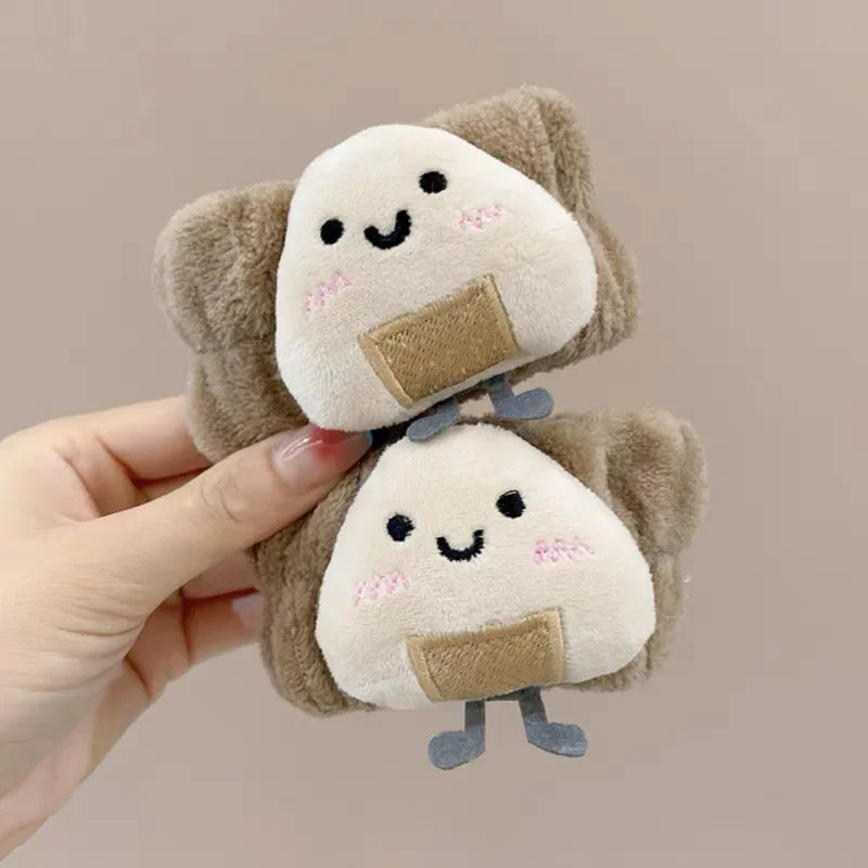 Mãos segurando dois brinquedos de pelúcia kawaii em formato de onigiri sorridentes e fofos