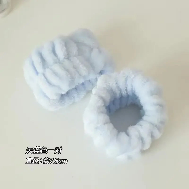 Par de elásticos de cabelo felpudos azul claro sobre superfície branca, diâmetro aproximado 7,5 cm