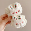 Mãos segurando coelho branco de pelúcia com bordados de cerejas e olhos fechados