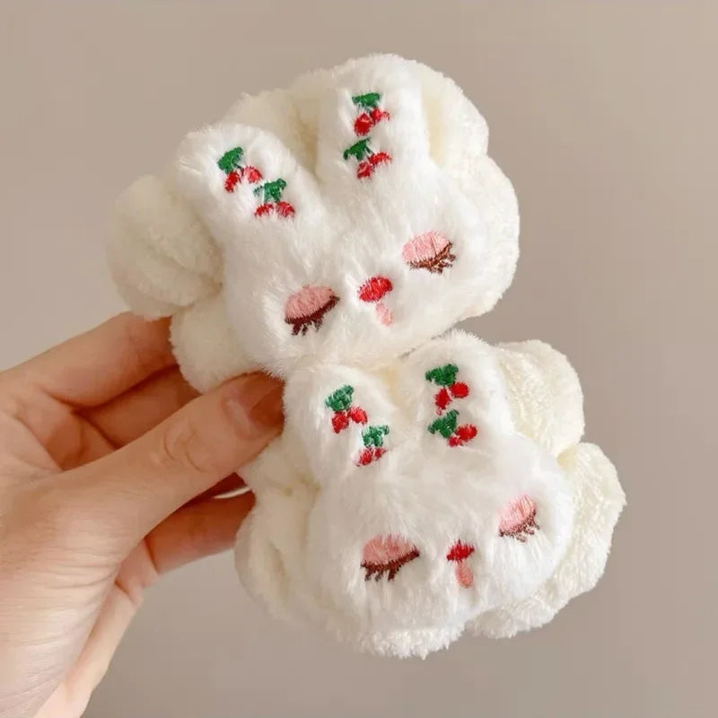 Mãos segurando coelho branco de pelúcia com bordados de cerejas e olhos fechados