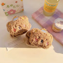 Meias felpudas marrom com rosto de ursinho e chapéu, sobre mesa com bebidas e papel decorativo