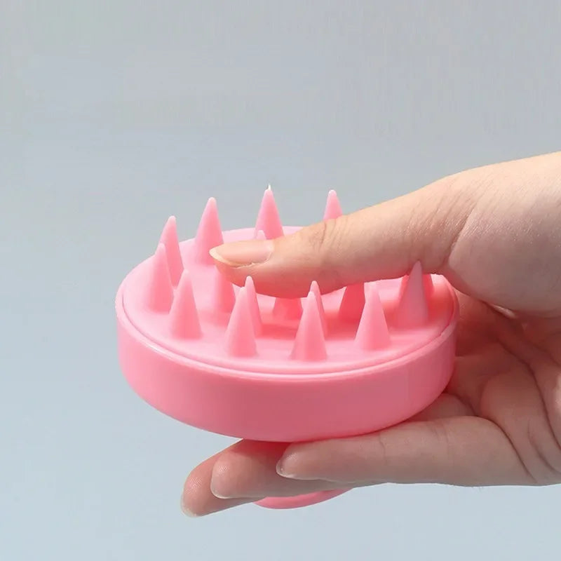 Mão segurando massageador de couro cabeludo rosa com pontas flexíveis para cuidado capilar