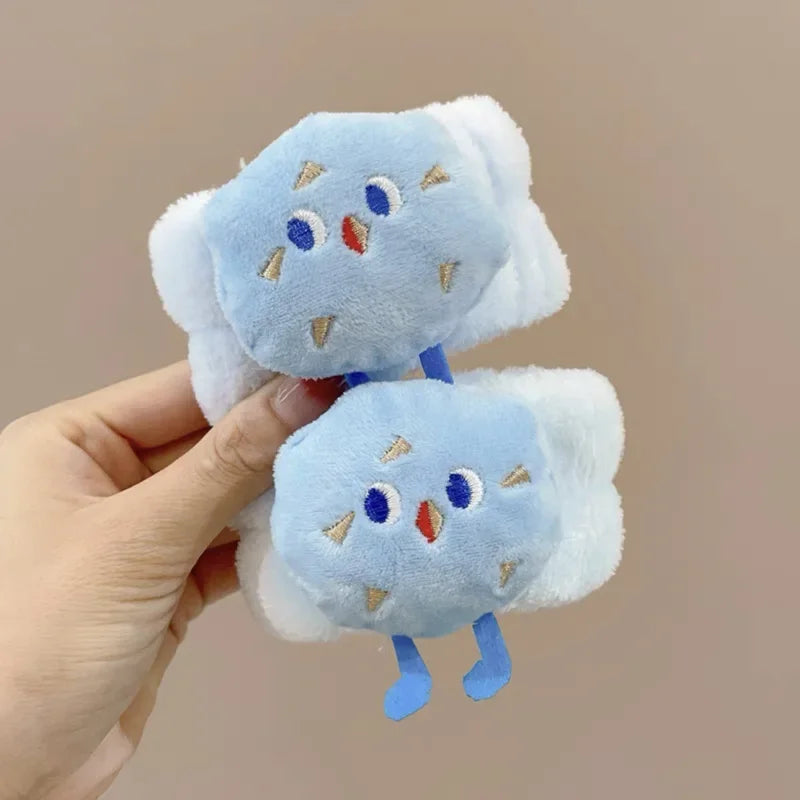 Mão segurando prendedores de cabelo de pelúcia azul com rosto de pássaro e pernas azuis